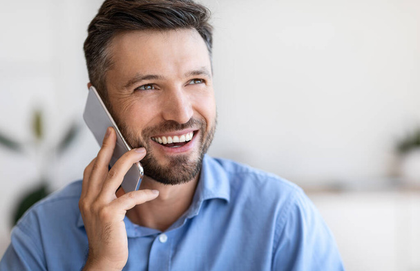 Close-up portret van lachende knappe jonge zakenman praten op mobiele telefoon binnen - Foto, afbeelding