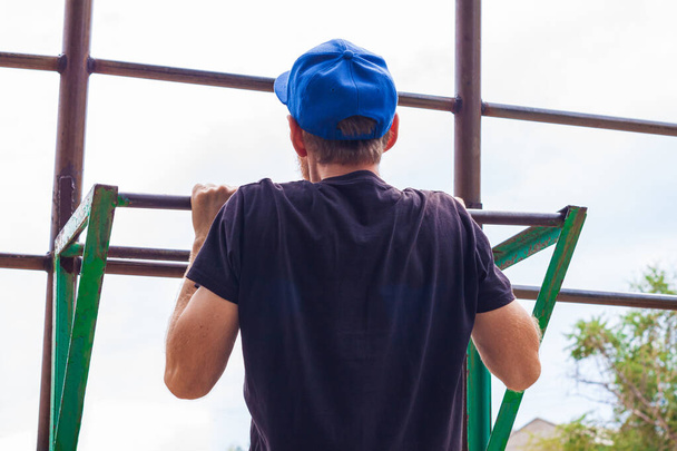 Athlete doing pull-up on horizontal bar. Male sportsman doing fitness exercises on playground outdoor during work break. Bearded young man with backpack warming up after working day. Active lifestyle. - Foto, immagini