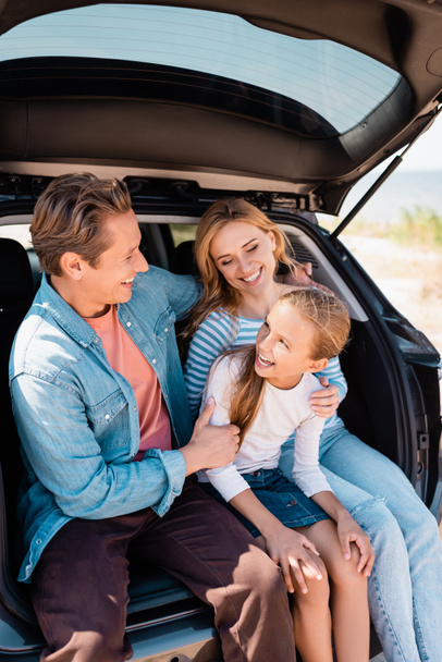 Selective focus of kid sitting near mother and father in car trunk outdoors  - Zdjęcie, obraz