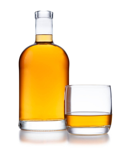 Ένα γεμάτο μπουκάλι σε σχήμα καμπάνας με χρυσό ουίσκι, χωρίς ετικέτα ή σήμα, και ένα ποτήρι ουίσκι, απομονωμένο στο λευκό με μια μικρή αντανάκλαση. - Φωτογραφία, εικόνα