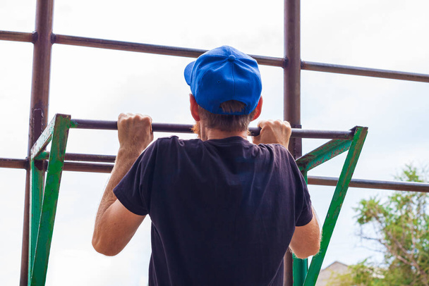 Athlete doing pull-up on horizontal bar. Male sportsman doing fitness exercises on playground outdoor during work break. Bearded young man with backpack warming up after working day. Active lifestyle. - Foto, Imagem