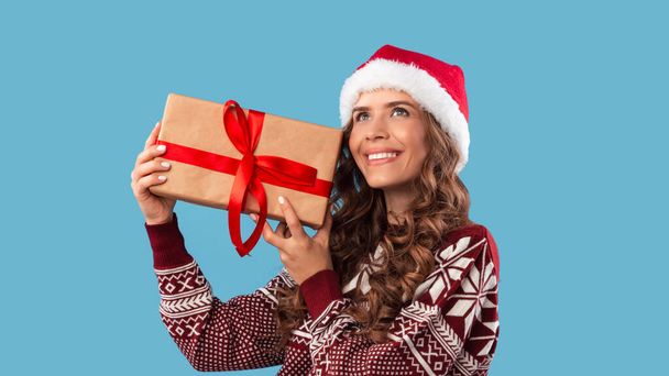 Weihnachtseinkäufe. Hübsche Millennial-Frau mit großem Weihnachtsgeschenk auf blauem Hintergrund - Foto, Bild