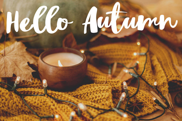 Hola otoño, texto escrito a mano sobre fondo de calabaza, hojas de otoño, vela, luces cálidas en suéter de punto amarillo. Acogedora caída - Foto, imagen