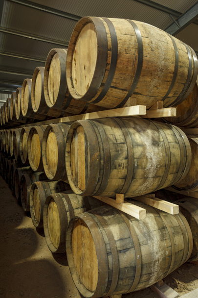 Una fila de pilas de barriles tradicionales de whisky, listos para madurar, en una gran instalación de almacén - Foto, Imagen