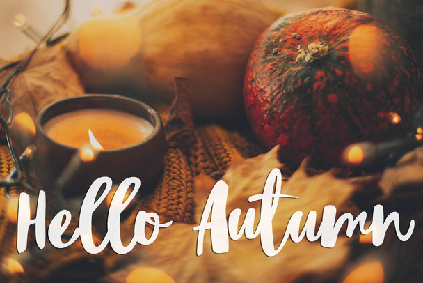 Hallo herfst wenskaart. Handgeschreven Hallo herfst tekst op de achtergrond van pompoen, herfst bladeren, kaars, warm licht op geel gebreide trui. Selectieve focus - Foto, afbeelding