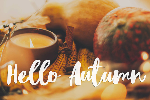Hola otoño, texto escrito a mano sobre fondo de calabaza, hojas de otoño, vela, luces cálidas en suéter de punto amarillo. Acogedor otoño, enfoque selectivo - Foto, imagen