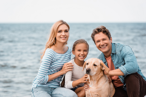 Famiglia con golden retriever che guarda la macchina fotografica sulla spiaggia  - Foto, immagini