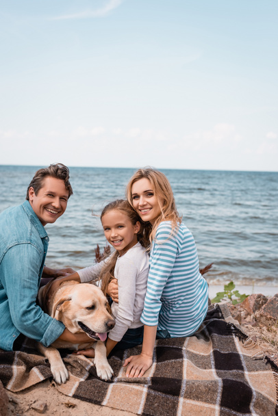 Family with golden retriever looking at camera while sitting on blanket  - Foto, immagini