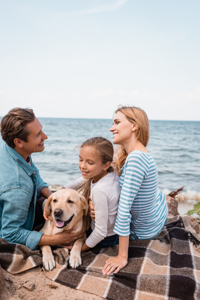 Parents looking at each other near golden retriever and child on seaside  - Fotoğraf, Görsel