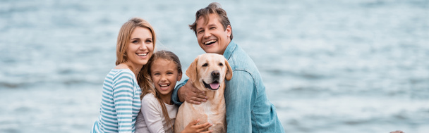 Panoramic shot of family embracing golden retriever on beach  - Foto, afbeelding