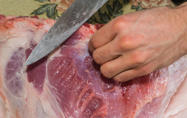 Ręka mężczyzny krojąca świeży surowy kawałek mięsa nożem, rzeźnia mięsa. - Zdjęcie, obraz