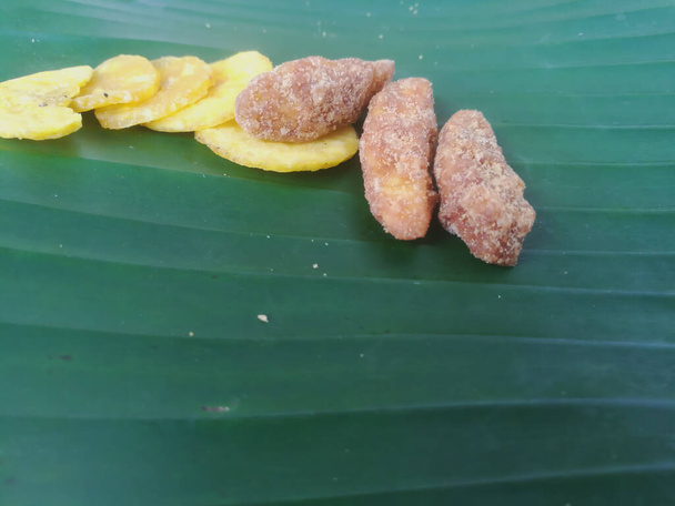 バナナの葉にジャギーコーティングされたバナナチップを持つバナナチップ。チップは黄色をしており、ジャギーコーティングされたチップは茶色です。. - 写真・画像