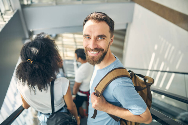 Gelukkige lachende man met baard op bewegende trap op internationale luchthaven - Foto, afbeelding