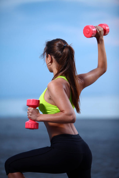 Beautiful woman doing exercises with dumbbells on the beach - Foto, Imagen