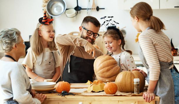 счастливая мать семьи, отец, бабушка и дети готовятся к Хэллоуину, вырезая тыквы дома на кухне - Фото, изображение