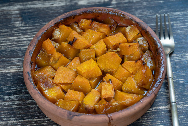 Baked yellow pumpkin with honey, olive oil and spices on a plate on the wooden table. Vegetarian food. Close up - Foto, Bild