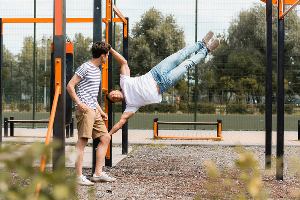 selectieve focus van tiener zoon kijken naar sportieve vader oefenen op horizontale balken  - Foto, afbeelding