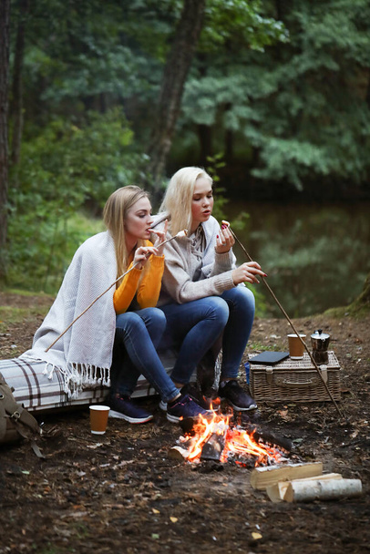 Travel and explore. Two young beautiful women near bonfire in the forest - Foto, imagen