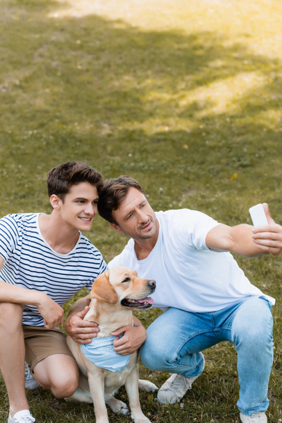 father and teenager son taking selfie with golden retriever in park - Foto, immagini