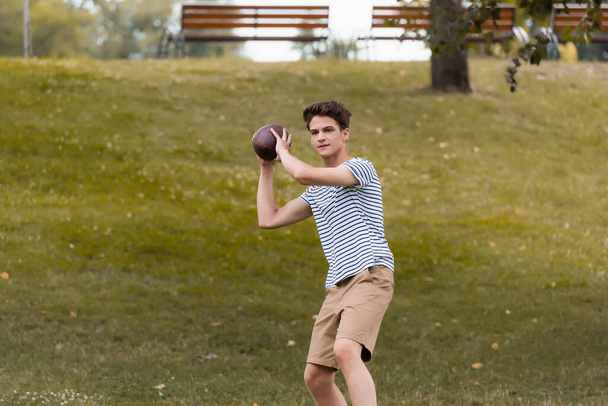 έφηβος αγόρι παίζει αμερικανικό ποδόσφαιρο στο πράσινο πάρκο - Φωτογραφία, εικόνα