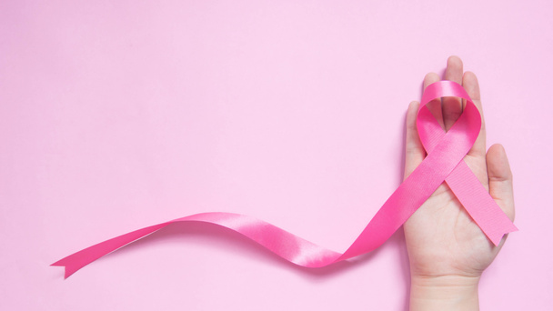 Mezinárodní symbol měsíce povědomí o rakovině prsu v říjnu. Detailní záběr ženské ruky drží saténově růžové stuhy vědomí na růžovém pozadí w / kopírovat prostor. Zdravotní péče pro ženy a lékařská koncepce. - Fotografie, Obrázek