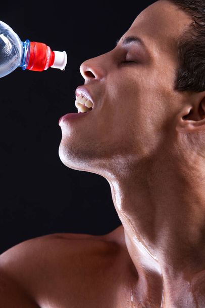 Young guy with bottle of cold water over black background - Photo, image
