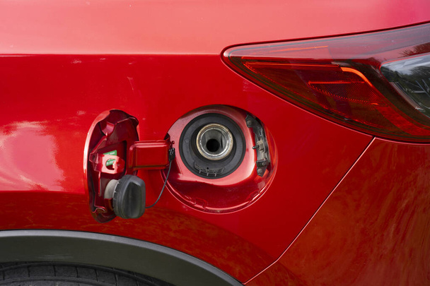 Ένα ανοικτό καπάκι δεξαμενής καυσίμου ενός κόκκινου αυτοκινήτου για την πλήρωση βενζίνης ή ντίζελ καυσίμου στη δεξαμενή αερίου. Το πίσω μέρος του αυτοκινήτου με μια ανοιχτή δεξαμενή αερίου. - Φωτογραφία, εικόνα