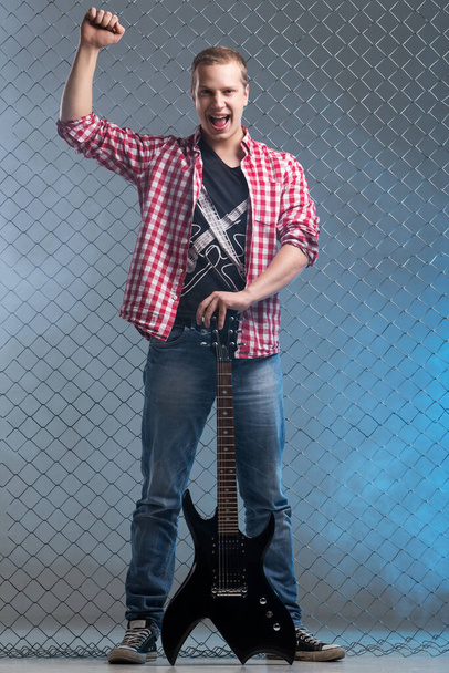Μουσική, ήχος. Μουσικός με κιθάρα σε φόντο φράχτη - Φωτογραφία, εικόνα