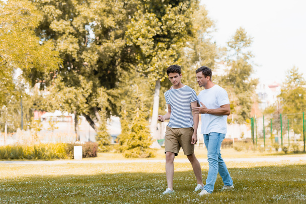 man gebaren terwijl wandelen en praten met tiener zoon in park  - Foto, afbeelding