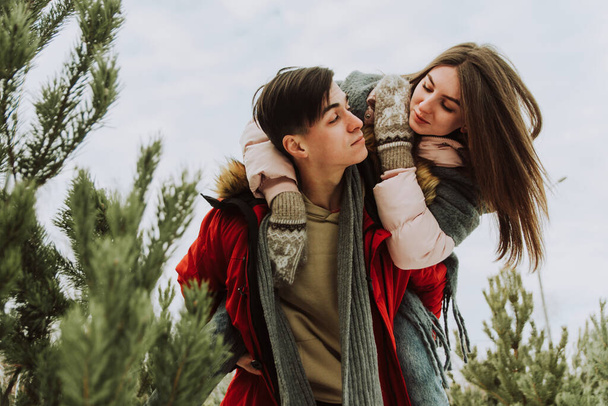 Ein schönes junges Paar kam, um einen Baum auszuwählen. Verliebte Frischvermählte albern im Winter herum. Eine hübsche Frau lacht auf den Schultern eines Mannes. - Foto, Bild