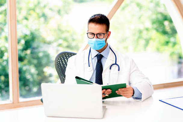 Portrait of male doctor wearing face mask for prevention while sitting and chechking appointments in his diary.  - Photo, Image
