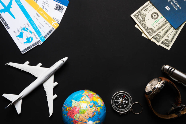 avion, globe, passeport, dollars, boussole horloge loupe sur fond noir concept de voyage - Photo, image