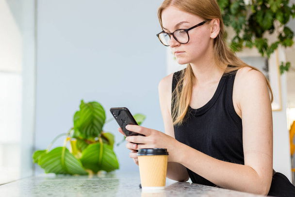 Kaunis nainen kahvilassa matkapuhelimella ja tekstiviestillä sosiaalisissa verkostoissa, Nainen freelancer juo kahvia. Ota pois käsite. - Valokuva, kuva