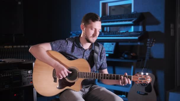 handsome talented guy with a beard plays an acoustic guitar in a music studio. Medium long shot - Footage, Video