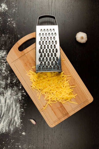 strouhaný čerstvý aromatický sýr na pizzu, česnek a strouhanku leží na dřevěné kuchyňské desce - Fotografie, Obrázek