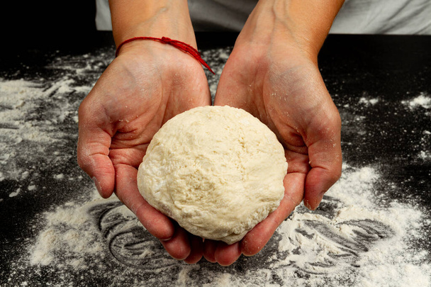 fille chef faire maison pâte à levure fraîche pour faire de la pizza sur fond de table en bois noir - Photo, image
