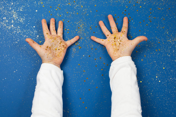 Child's hands holding golden stars on sparkling blue background. Bright Christmas and New Year picture. flat lay. Top view, flat lay - Photo, image