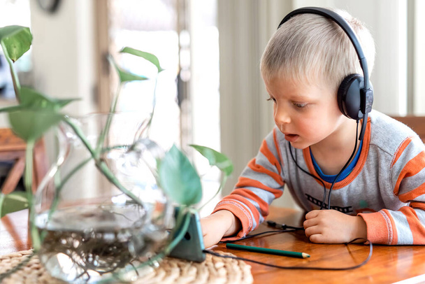 Маленький хлопчик робить навушники і грає на мобільному телефоні
 - Фото, зображення