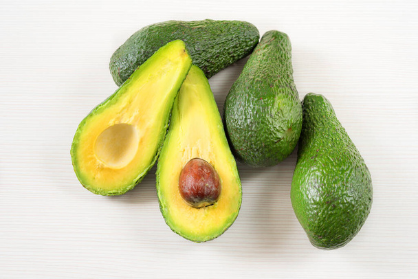 Close-up photo of avocados cut to half, brown seeds visible, with more avocados on white wooden background. Fresh sliced avocado.Vegetarian food concept. - Photo, Image