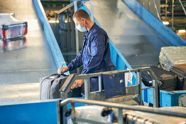 Uomo in tuta che controlla una targhetta sui bagagli dei passeggeri - Foto, immagini