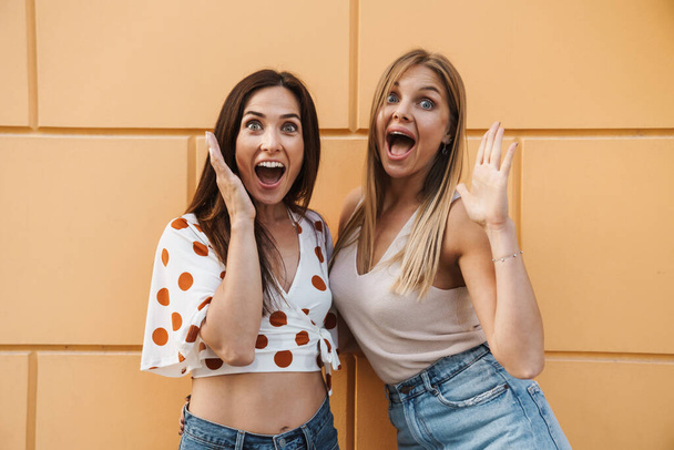 Image of excited adult two women hugging and expressing surprise while posing on city street - Photo, Image