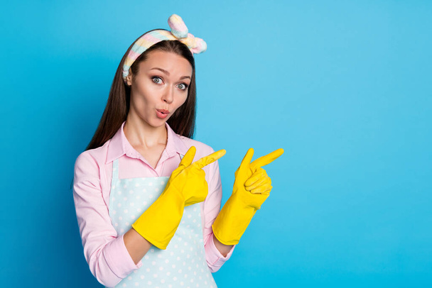 Portrait of shocked astonished girl cleaner pint index finger copyspace rubber gloves demonstrate incredible ads promotion impressed wear pink shirt isolated over blue color background - Фото, зображення