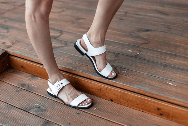 Woman in trendy leather casual white sandals poses on the wooden floor. Close-up. - Фото, изображение