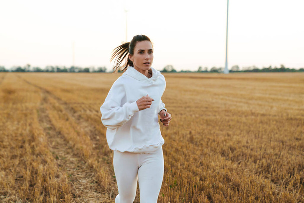 Image of adult beautiful sportswoman running while working out at golden field - Фото, зображення