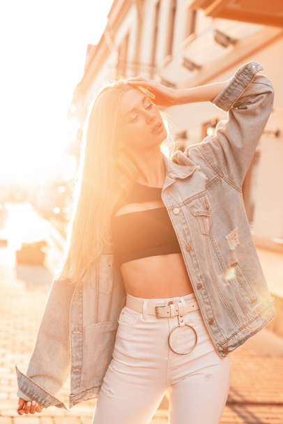 Moda ładna kobieta hipster w dżinsowej kurtce w białych dżinsach vintage korzystających o zachodzie słońca  - Zdjęcie, obraz