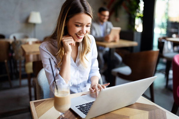 Portrait of a young beautiful businesswomen enjoying coffee during work on portable laptop computer - Foto, Bild