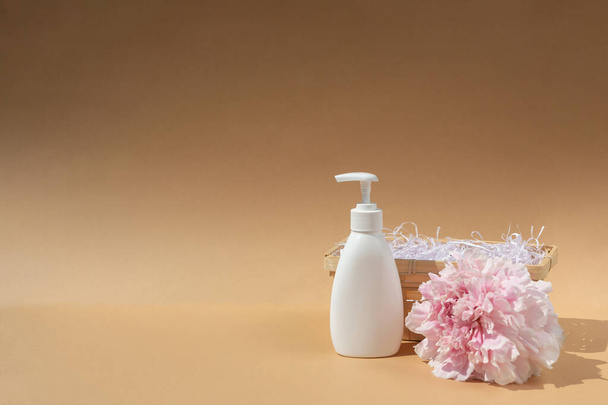 White bottle and wicker basket. Large bud of pink peony. Cosmetics and perfumery. Body and skin care. Spa concept, massage. Place for your text. - Foto, immagini