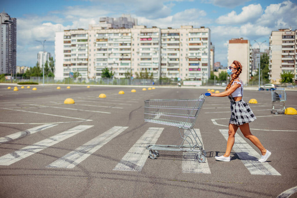 Supermarket trolley. A woman in a medical mask carries a supermarket trolley. - Фото, изображение
