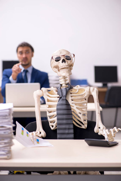 Młody pracownik płci męskiej ze szkieletami w biurze - Zdjęcie, obraz