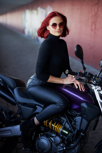 Koyu renkli motosikletle poz veren kızıl saçlı bir kız. - Fotoğraf, Görsel